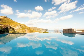 A clear blue infinity pool with a view of a mountainous landscape and a building in the distance.