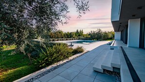 A modern outdoor pool area with a clear view of the sky, surrounded by well-maintained greenery and a paved walkway. - Martincic Residence (Marcana)