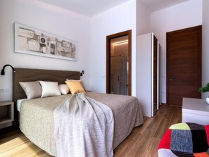 A modern bedroom with a large bed, a nightstand, a wall-mounted lamp, and a door leading to a bathroom. - Martincic Residence (Marcana)
