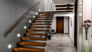 A modern staircase with wooden steps and glass railings, leading to a hallway with a tiled floor and a door at the end. - Martincic Residence (Marcana)