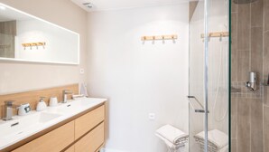 Een moderne badkamer met een glazen douchecabine, een grote spiegel en een houten wastafelmeubel met meerdere wasbakken.