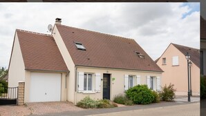 Een gelijkvloers huis met zadeldak, een garage en een kleine voortuin met struiken.