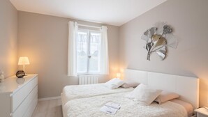 Een slaapkamer met twee bedden, een raam met gordijnen, een nachtkastje met een lamp en een decoratief object aan de muur.