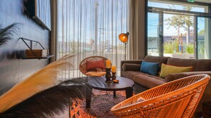 A modern living room with a sofa, two wicker chairs, a coffee table, and a large window with sheer curtains. - PLAZA INN Ulm (Ulm)