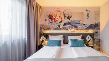 Hotellihuone, jossa on sänky, yöpöytä, lamppu ja seinämaalaus.