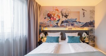 Una habitación de hotel con una cama, una mesita de noche, una lámpara y un mural en la pared.