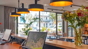 A modern hotel lobby with a wooden reception desk, a laptop, and a vase with flowers. - PLAZA INN Ulm (Ulm)