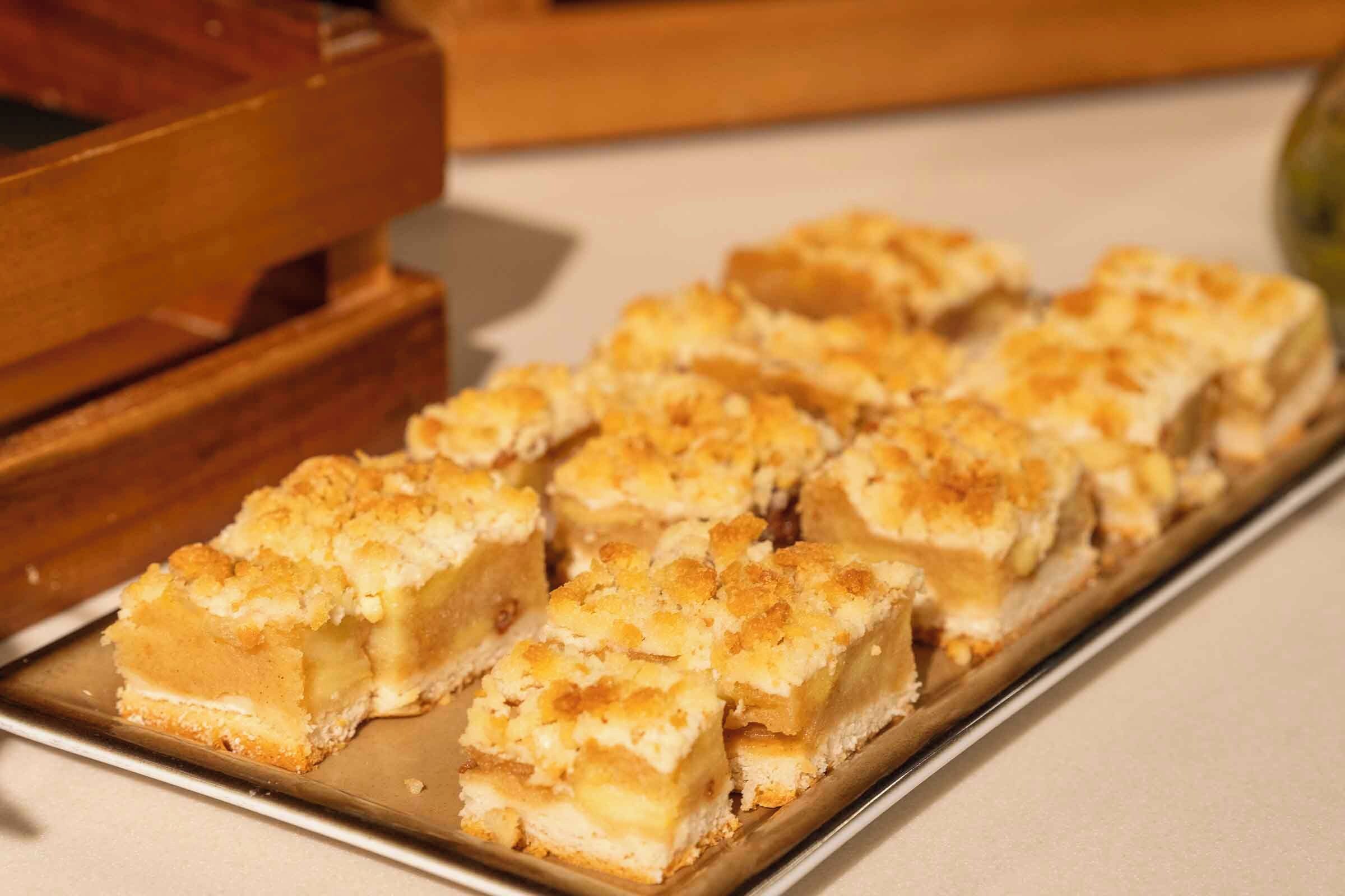 A tray of square-shaped desserts with a golden-brown crust, placed on a white surface.