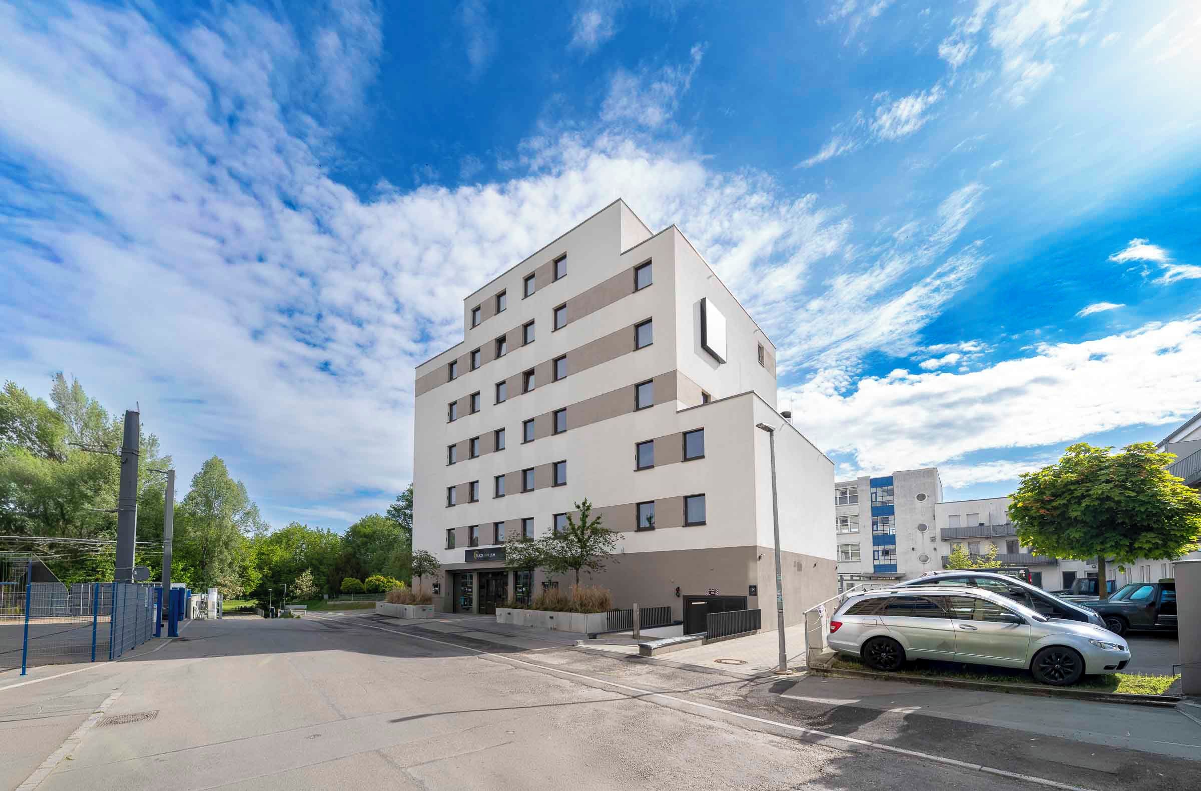 A multi-story building with a flat facade, a parking area, and a clear sky.