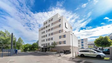 Un edificio de varios pisos con fachada plana, un área de estacionamiento y cielo despejado.