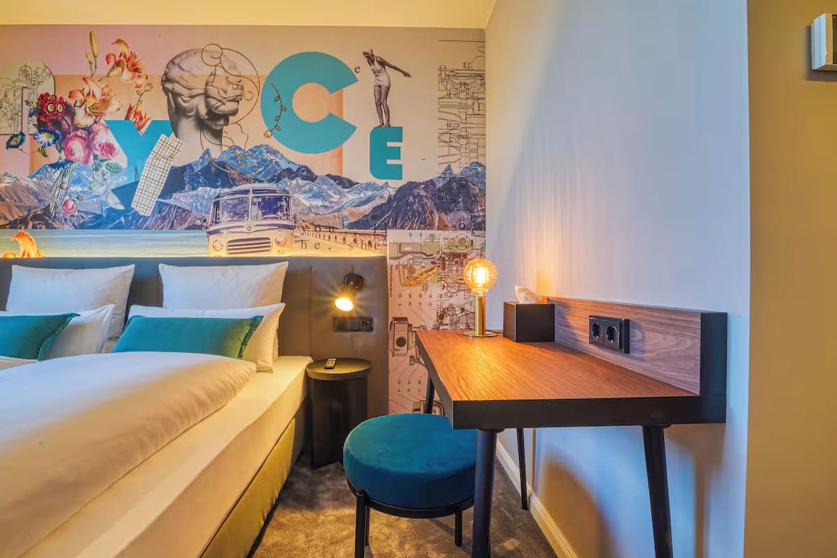 A hotel room with two beds, a desk, and a wall mural.