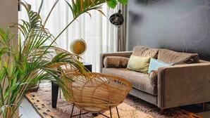 A living room with a sofa, a woven chair, a large plant, and a globe on a table. - PLAZA INN Ulm (Ulm)