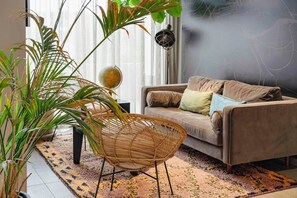 A living room with a sofa, a woven chair, a large plant, and a globe on a table. - PLAZA INN Ulm (Ulm)