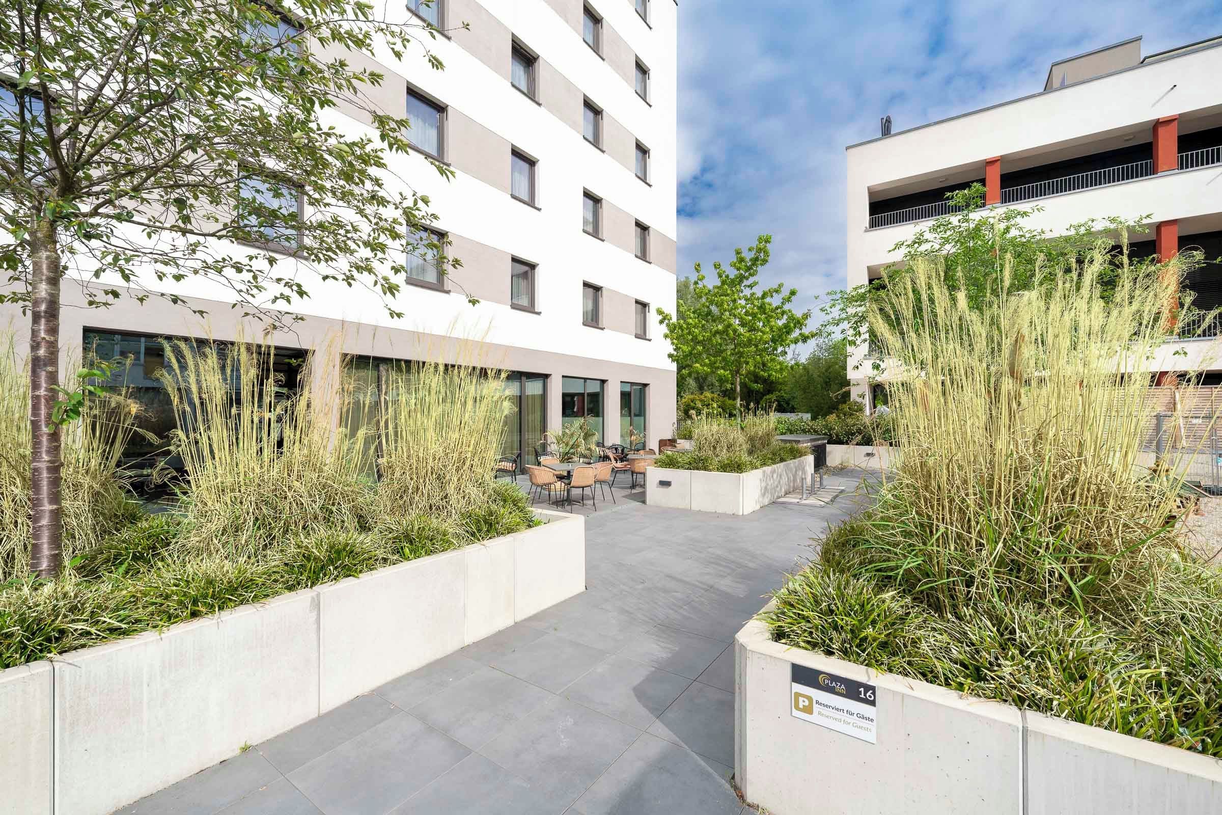 Un edificio moderno con un patio que incluye asientos al aire libre y macetas con pastos altos.