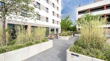 Un edificio moderno con un patio que incluye asientos al aire libre y macetas con pastos altos.