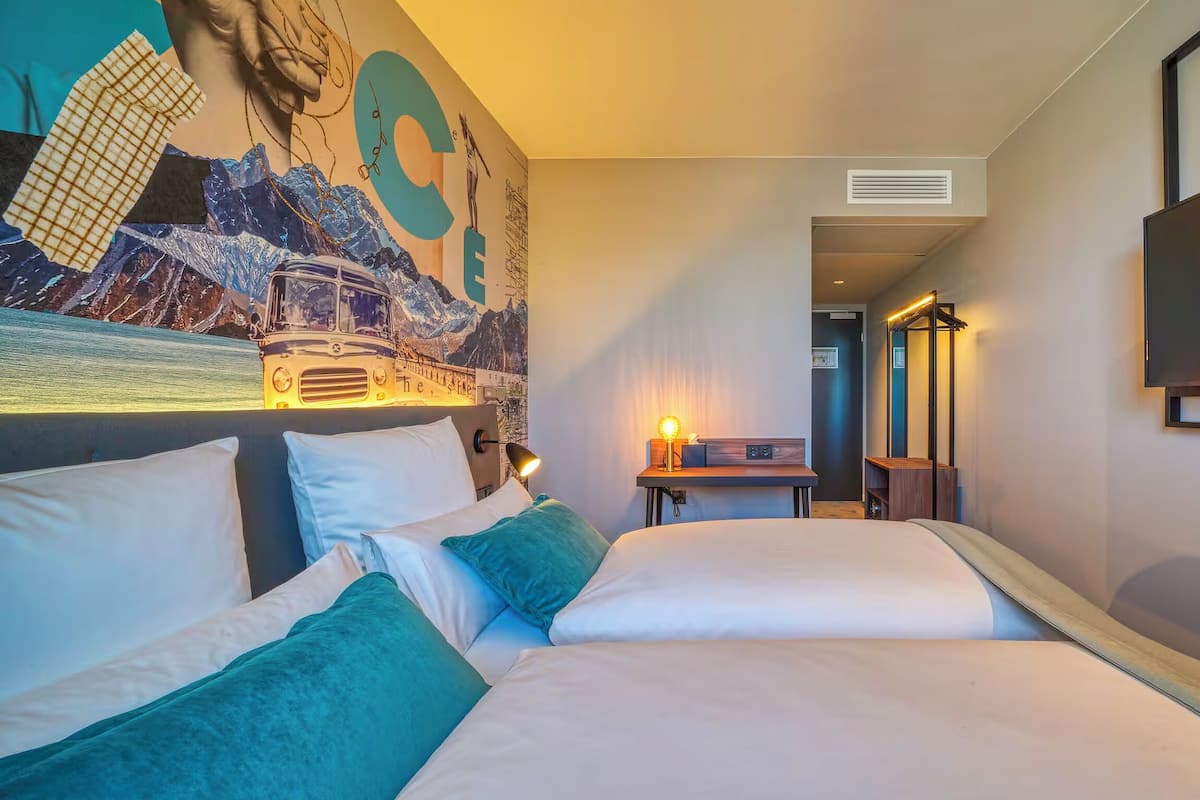 A hotel room with a bed, a desk, a television, and a mural on the wall.