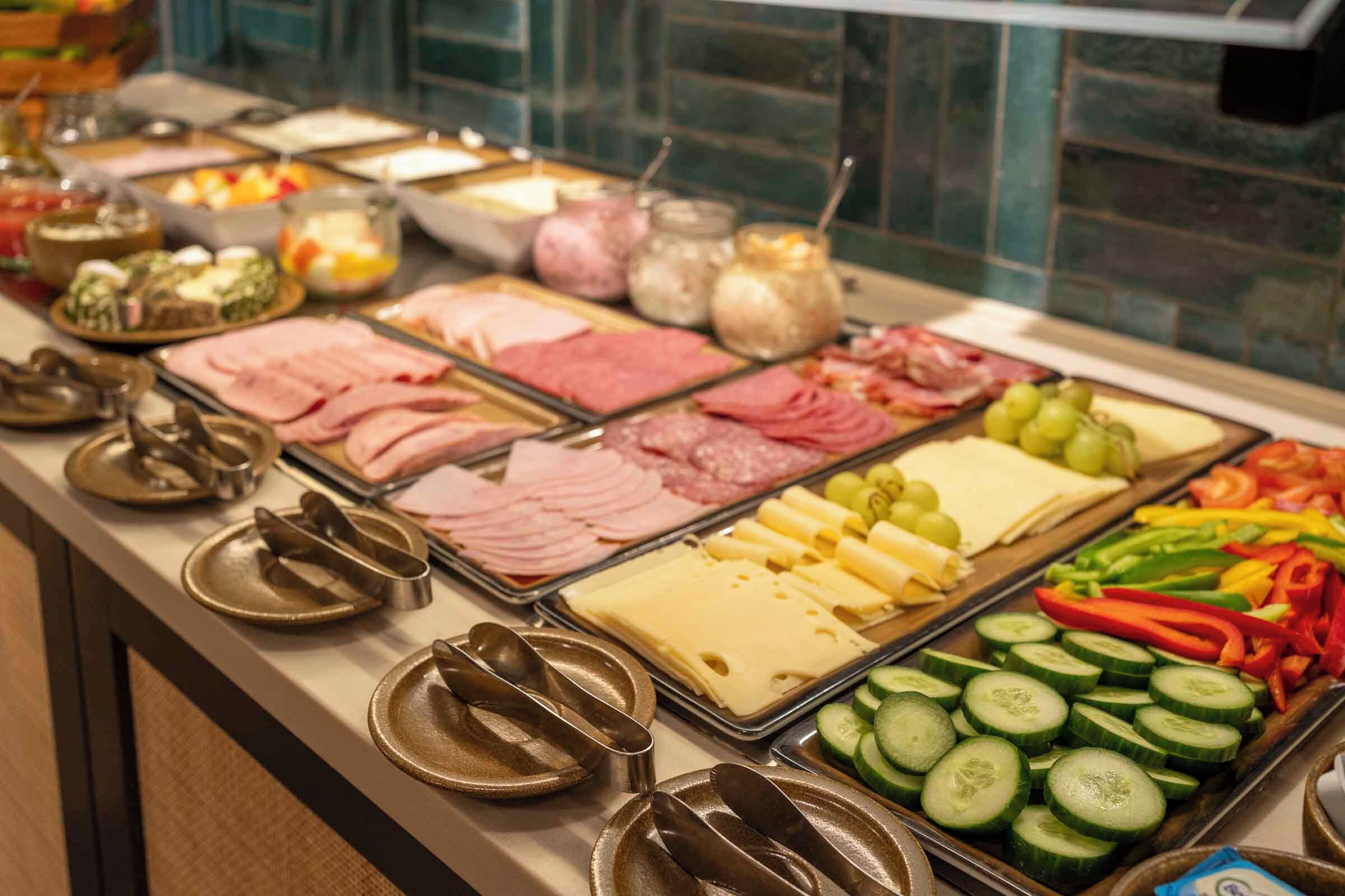A buffet with various food items including sliced meats, cheeses, and vegetables.