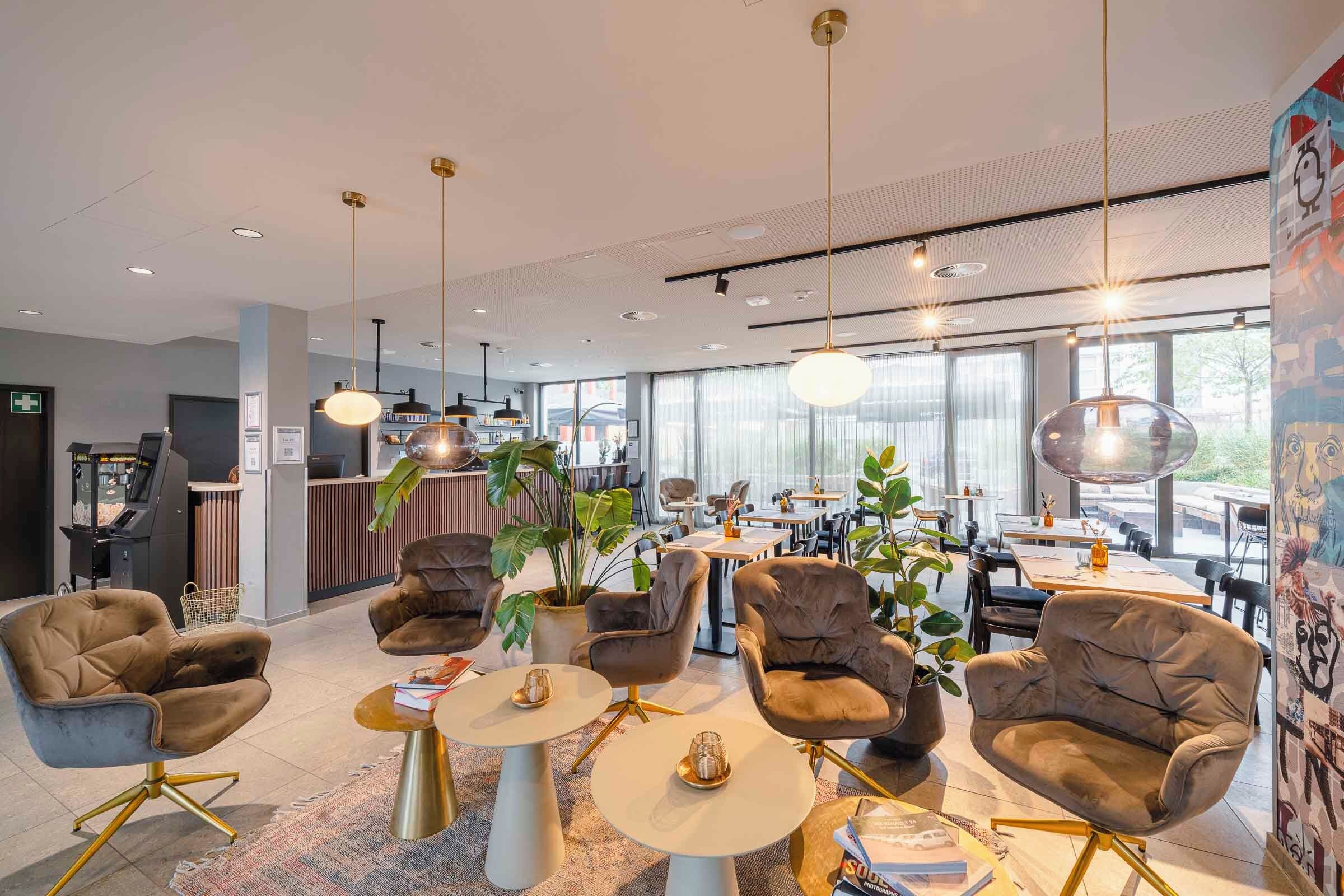 A modern hotel lobby with leather armchairs, round tables, and hanging pendant lights.