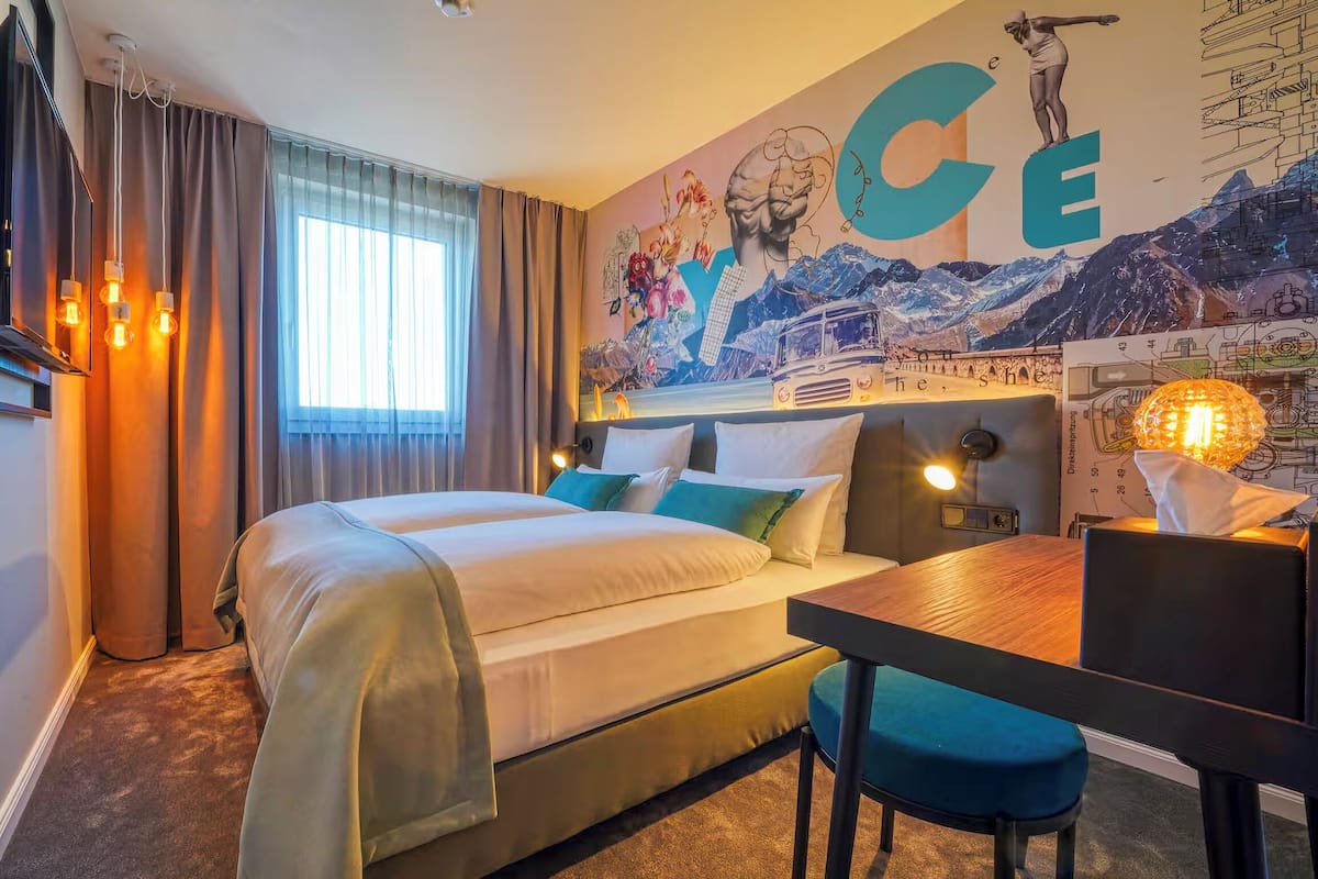 A hotel room with a bed, a desk, and a large wall mural.
