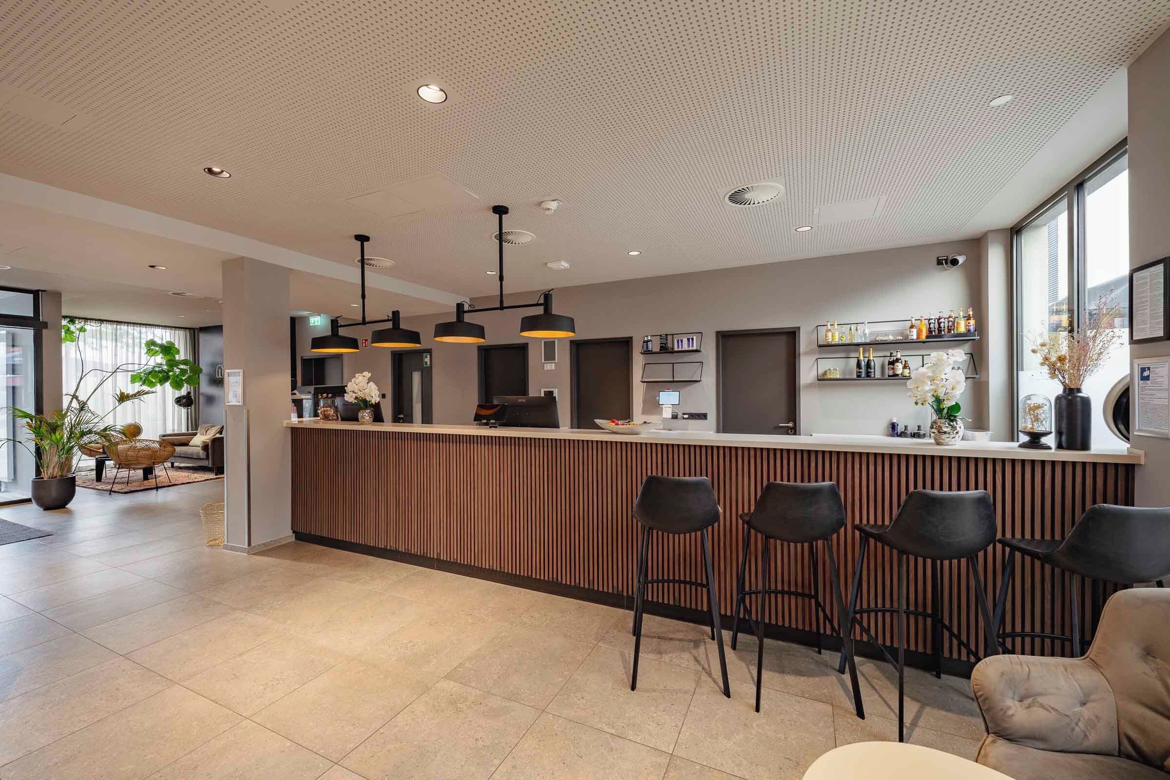 A modern bar area with a wooden counter, black bar stools, and pendant lighting.