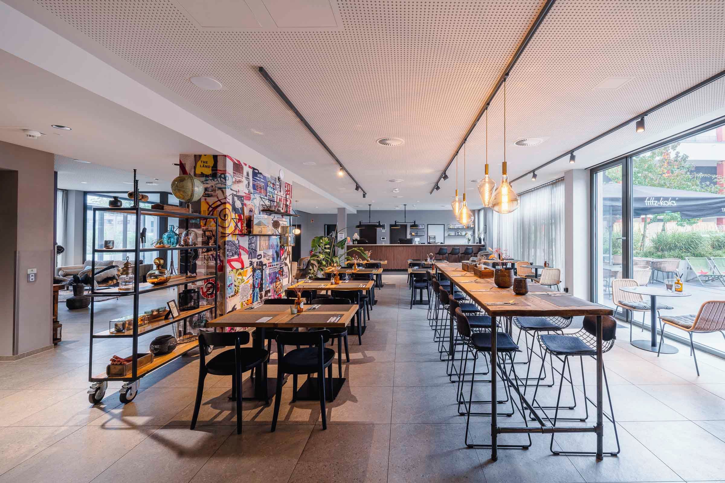 Interior de una cafetería moderna con techos altos, conductos expuestos y diversas opciones de asientos, incluyendo mesas y taburetes de bar.