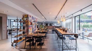 Interior de una cafetería moderna con techos altos, conductos expuestos y diversas opciones de asientos, incluyendo mesas y taburetes de bar.