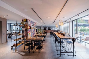 Interior de una cafetería moderna con techos altos, conductos expuestos y diversas opciones de asientos, incluyendo mesas y taburetes de bar.