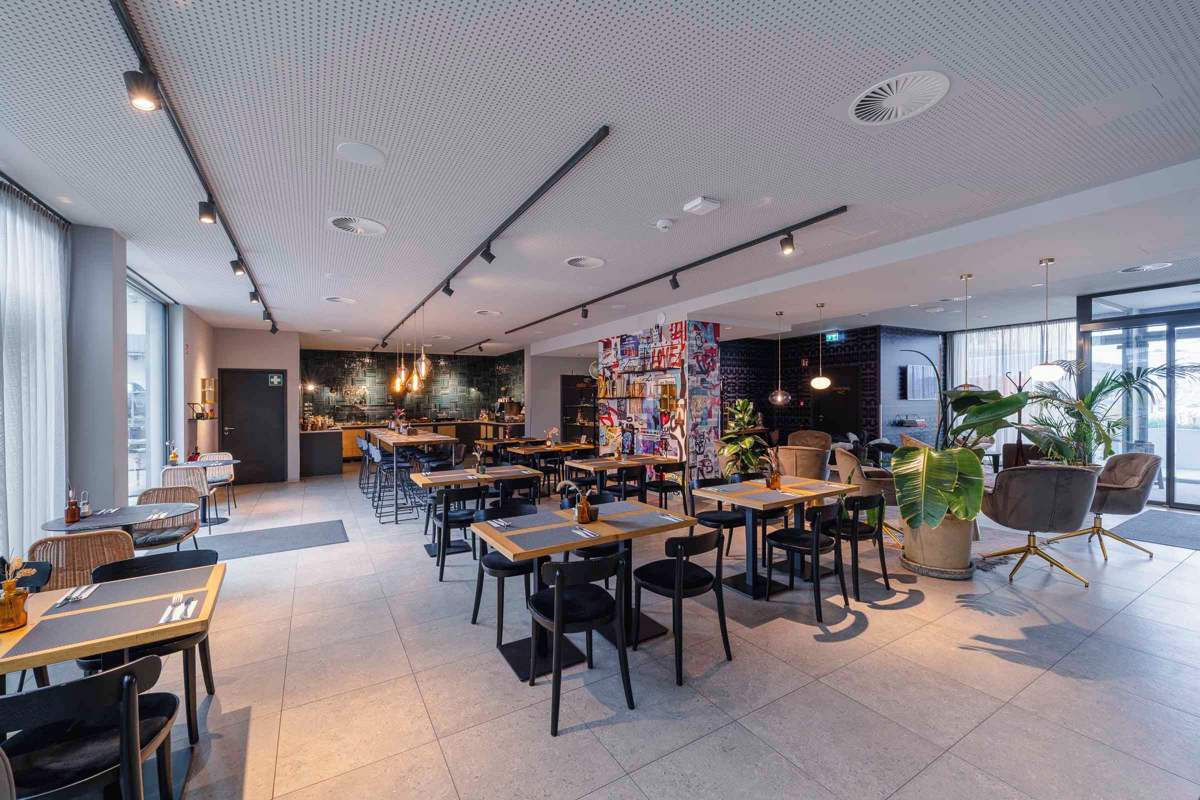 Ein modernes Restaurant mit hoher Decke, mehreren Essbereichen und Blick auf die Stadt.