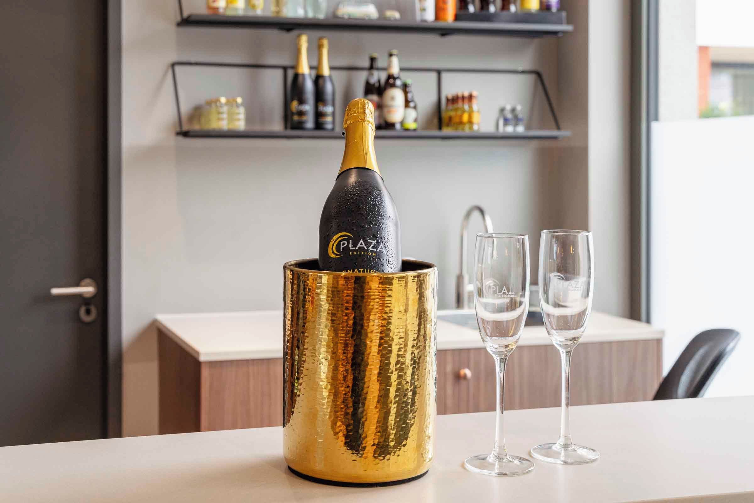 A champagne bottle in a golden container with two glasses beside it.