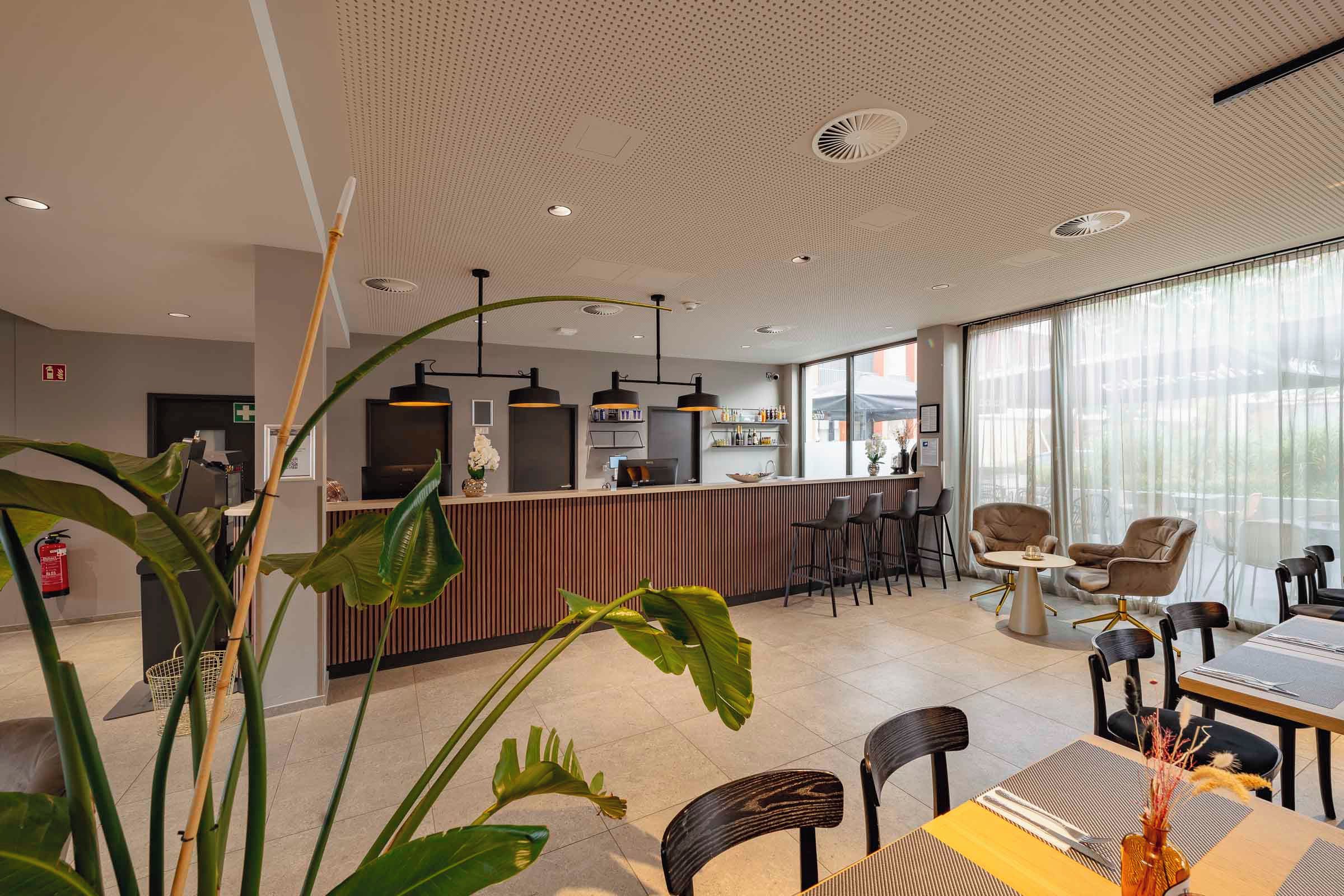 A modern hotel lobby with a reception desk, seating area, and large windows.