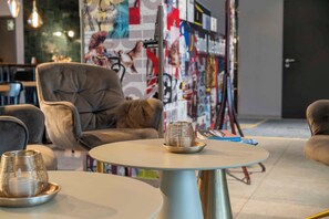 A modern lounge area with a round table, a cushioned armchair, and a decorative metal object on the table. - PLAZA INN Ulm (Ulm)