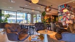 A modern lounge area with leather sofas, a round table, and a large wall of colorful artwork. - PLAZA INN Ulm (Ulm)