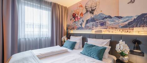 Una habitación de hotel con cama, mesita de noche, lámpara de pared y ventana con cortinas.