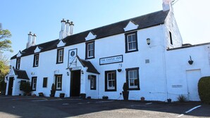 A white building with black trim, labeled "The Castle Inn," featuring a traditional architectural style with multiple chimneys and a prominent entrance. - The Castle Inn (North Berwick)