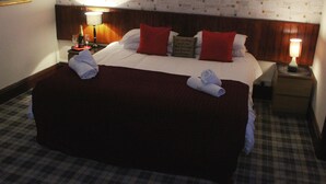 A hotel room with a large bed, two nightstands, a wooden headboard, and a checkered floor. - The Castle Inn (North Berwick)
