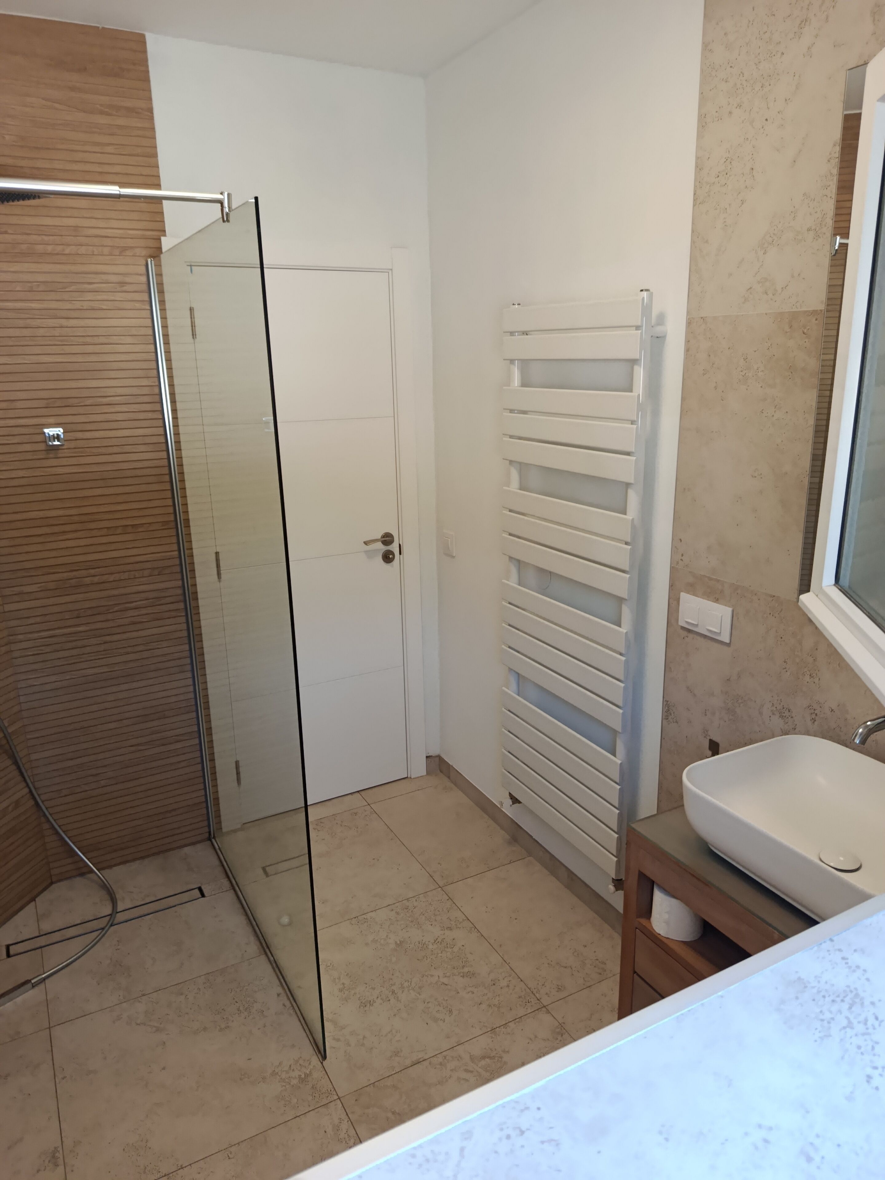 A modern bathroom with a glass shower enclosure, a white door, a towel rack, and a sink with a mirror.