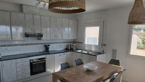 A modern kitchen with white cabinets, a wooden dining table, and a window providing natural light.