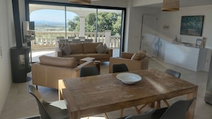A modern living room with a wooden dining table, leather sofas, and a large window offering a view of the outdoors.