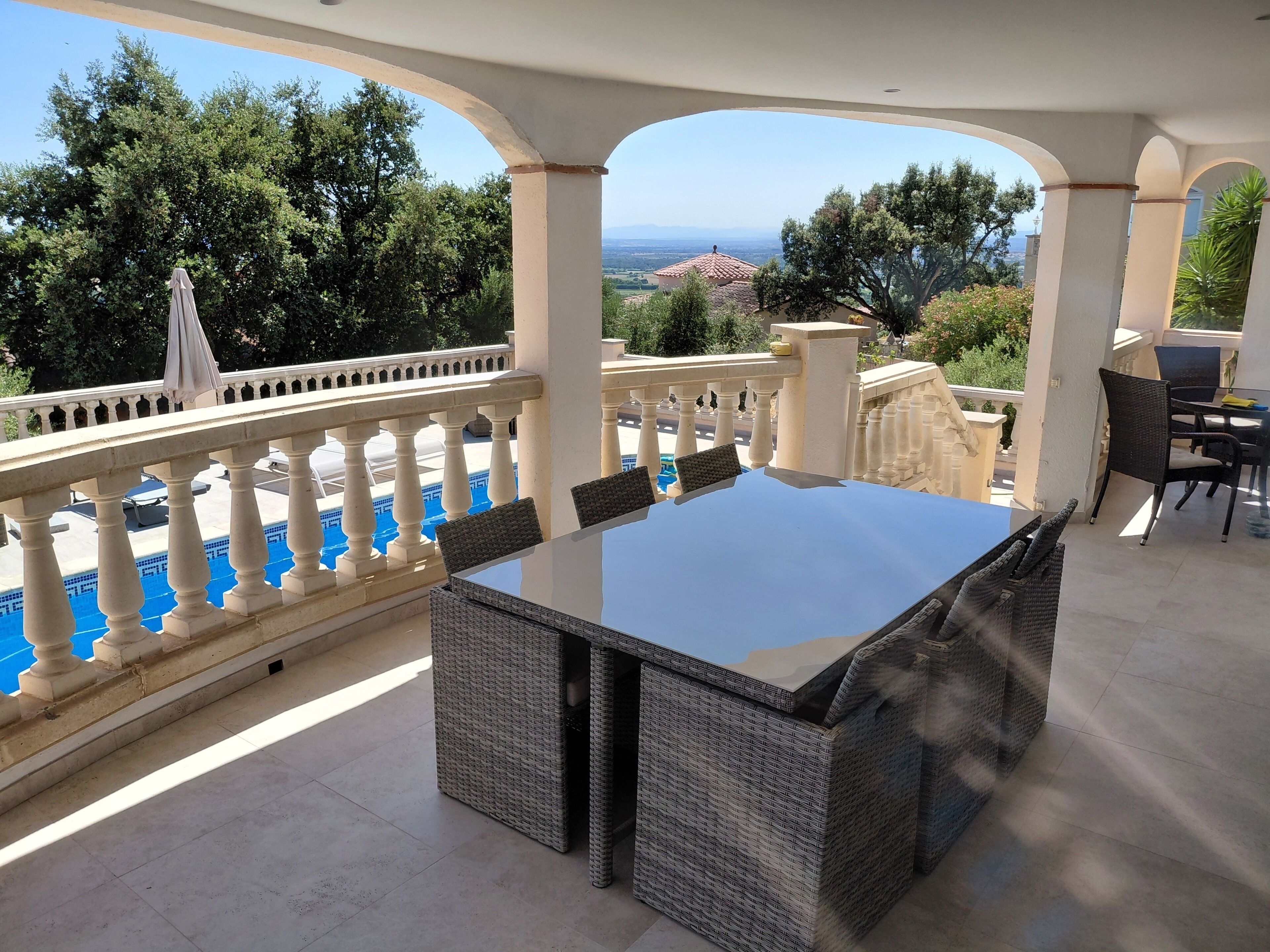 Un espace extérieur couvert aménagé pour les repas, avec vue sur la piscine, comprenant une table et des chaises, et offrant un panorama sur le paysage.