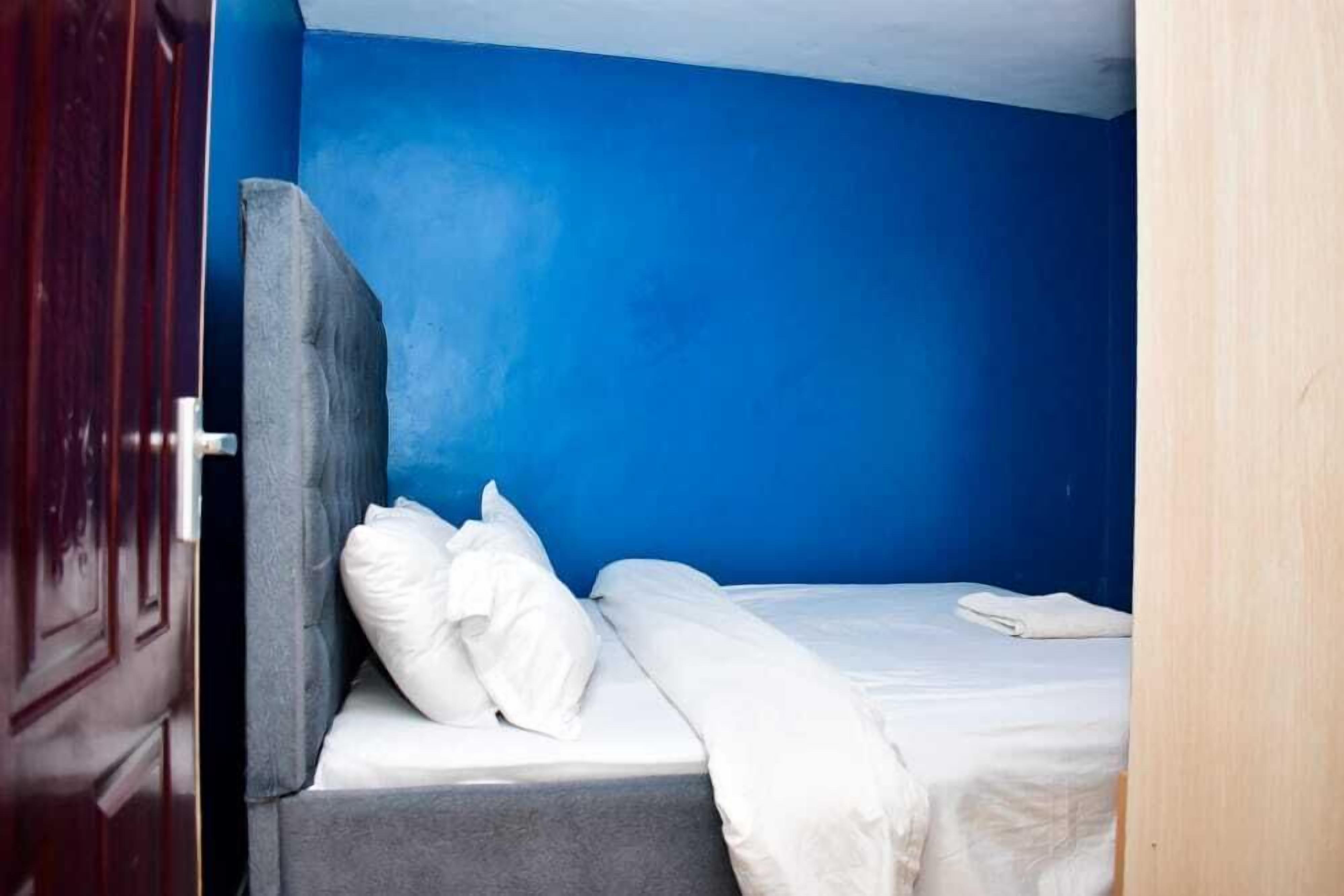 Un lit simple avec une literie blanche, dans une pièce aux murs bleus.