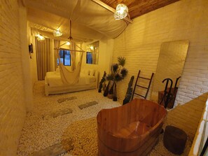 A spa room with a white brick wall, a wooden bathtub, a white sofa, and a large mirror. - Language Exchange Hotel 3 (Ho Chi Minh City)