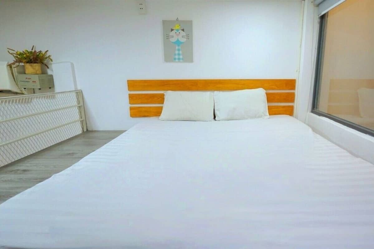 A bedroom with a large bed, a wooden headboard, a window with a view, and a small desk with a plant.