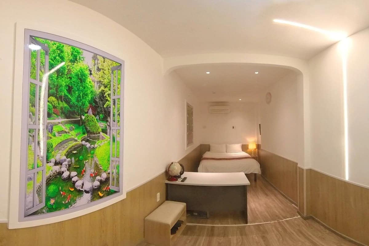 A hotel room with a bed, bedside table, and a large window with a view of a garden.