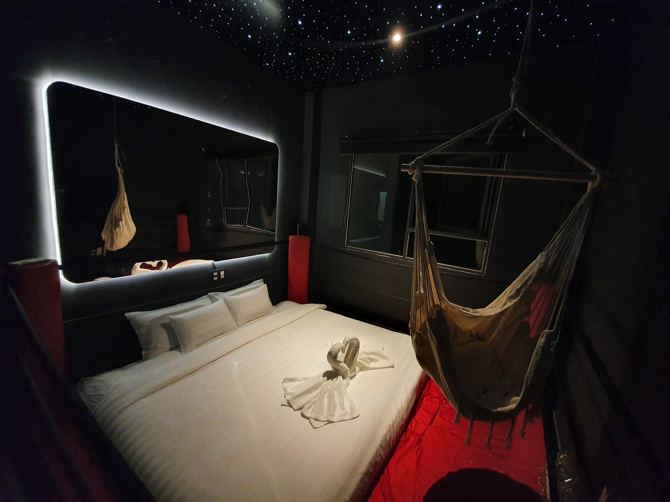 A modern bedroom with a large bed, a hanging hammock, and a starry ceiling.