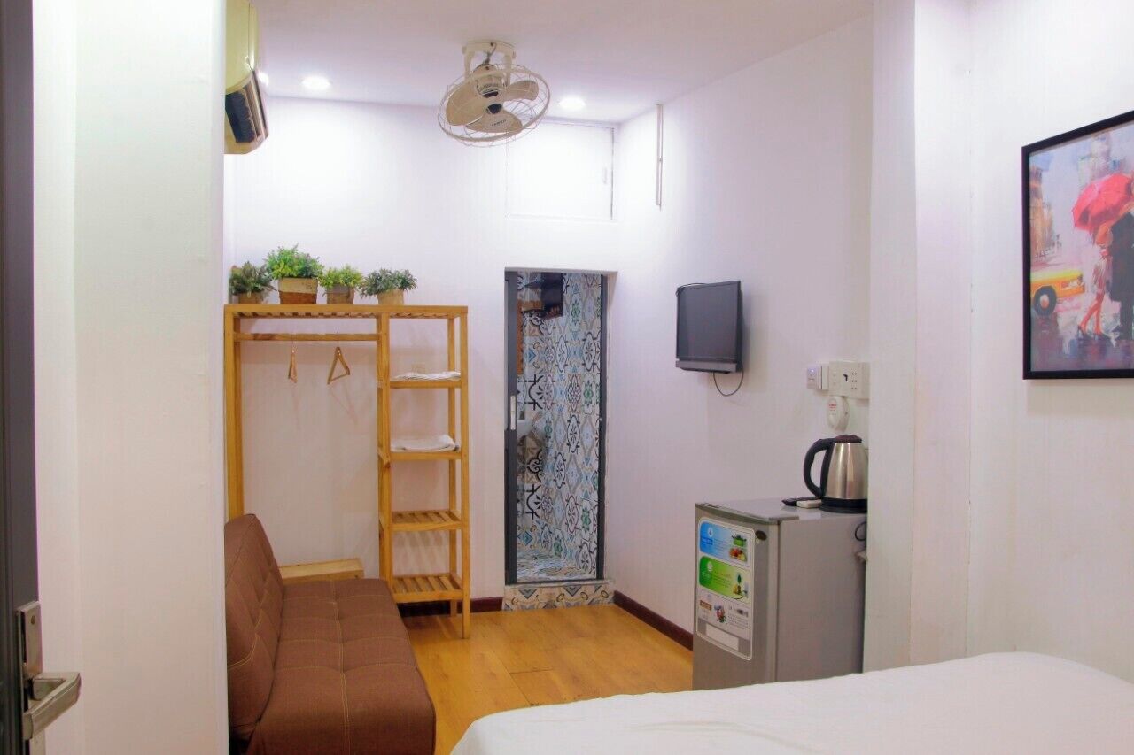 A hotel room with a bed, a wooden wardrobe, a small kitchenette, a television, and a painting on the wall.