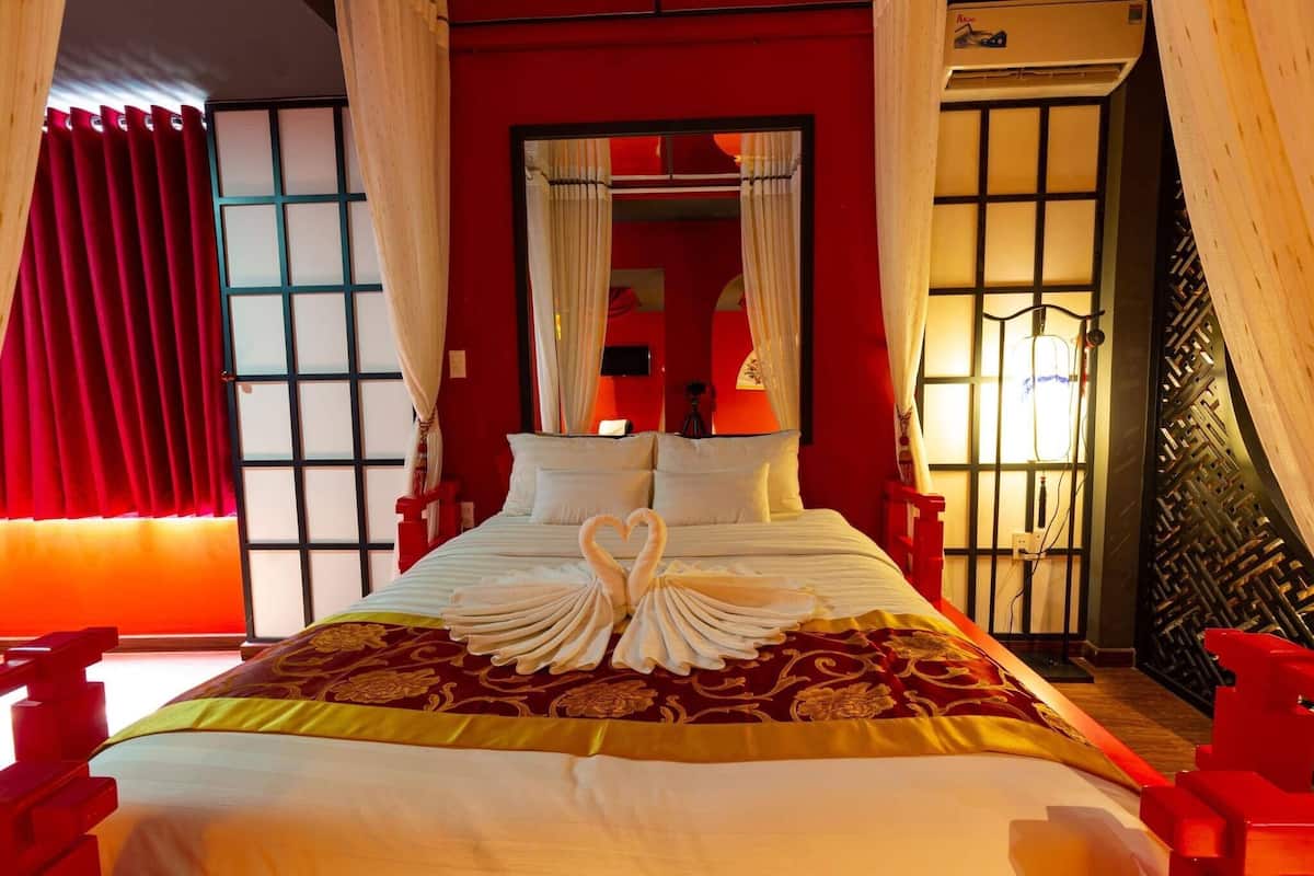 A hotel room with a bed, red curtains, a mirror, and a red wall.