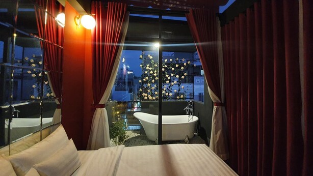 A bedroom with a large bed, a bathtub, and a window with curtains. - Language Exchange Hotel 3 (Ho Chi Minh City)