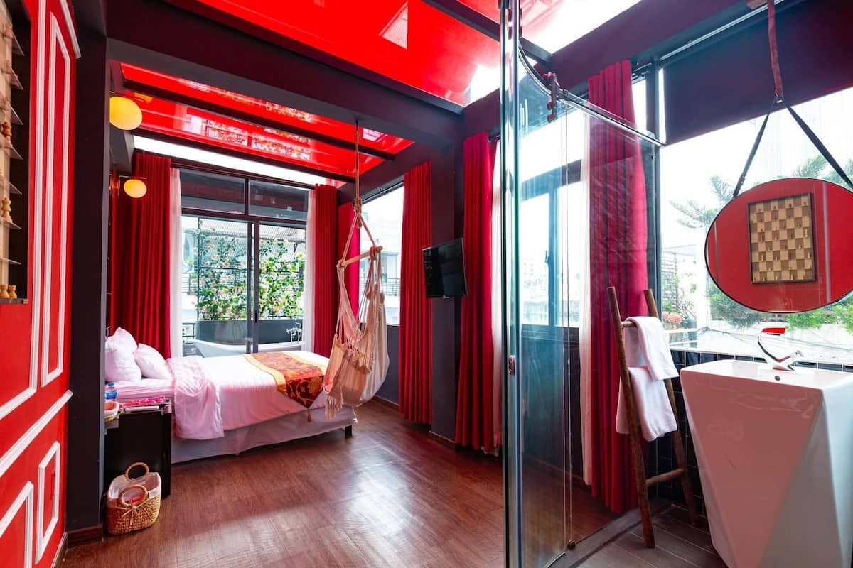 A hotel room with a bed, a small table, a chair, and a large window with curtains.