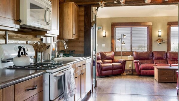 A kitchen with wooden cabinets, a stove, and a kettle. There is a leather sofa and a small table in the living area.