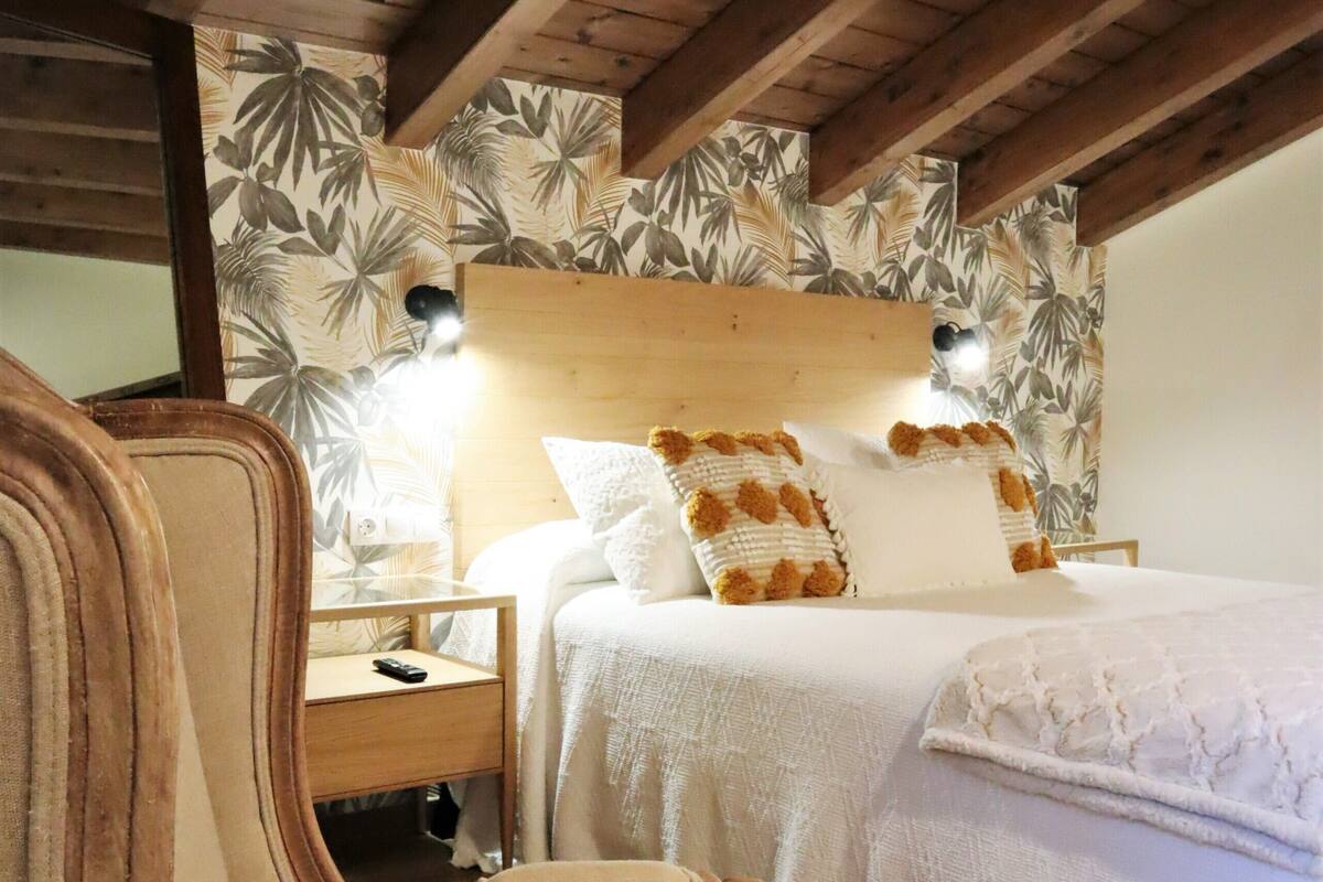 A bedroom with a wooden ceiling, a bed with white bedding, a nightstand, and a chair.